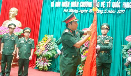 Thiếu tướng Phùng Sĩ Tấn gắn Huân chương bảo vệ Tổ quốc lên lá cờ Quyết chiến Quyết thắng của LLVT tỉnh Hà Giang.